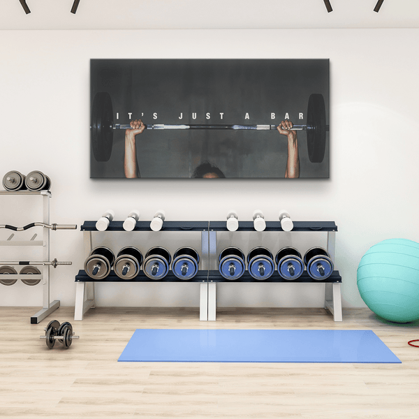 Motivational gym wall art reading 'IT'S JUST A BAR' above dumbbells and workout equipment