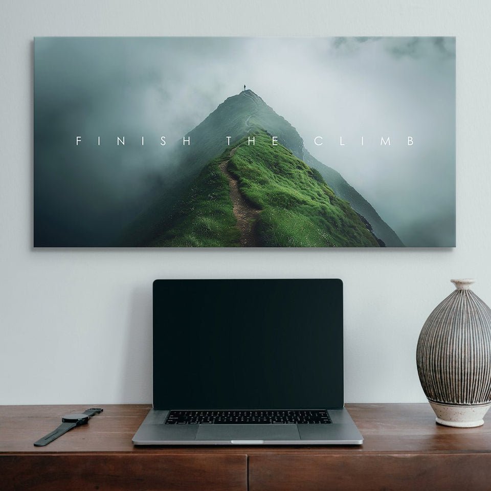 Motivational wall art with 'Finish The Climb' text, lush mountain peak, modern desk setup
